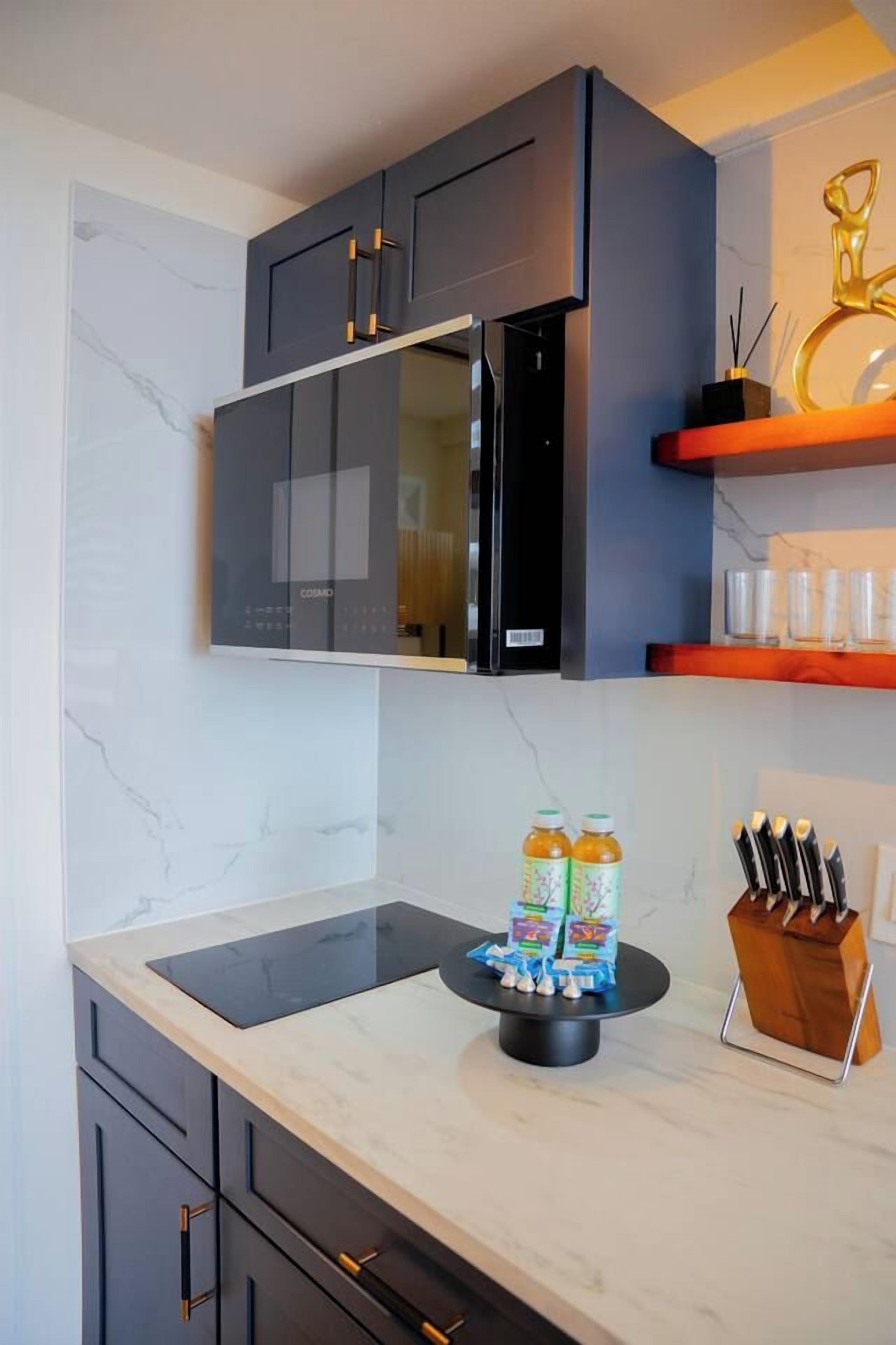 Een moderne keuken met donkere kastjes, een zwarte magnetron en een marmeren aanrecht.