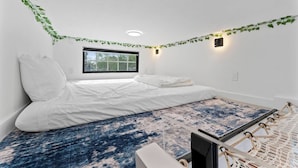 Et soveværelse med en seng, et vindue, en lampe på væggen og et tæppe med et mønster.
