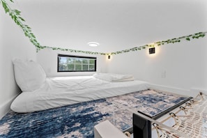 A bedroom with a bed, a window, a wall-mounted light, and a patterned rug. - Tiny House on Galveston Bay | Pier + Bay Views (Bacliff)