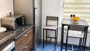 A compact kitchen with a refrigerator, stove, microwave, and a small dining area with a chair and table.