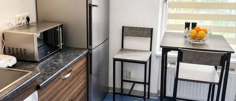 Une cuisine compacte équipée d’un réfrigérateur, d’une cuisinière, d’un four à micro-ondes et d’un petit coin repas avec une chaise et une table.