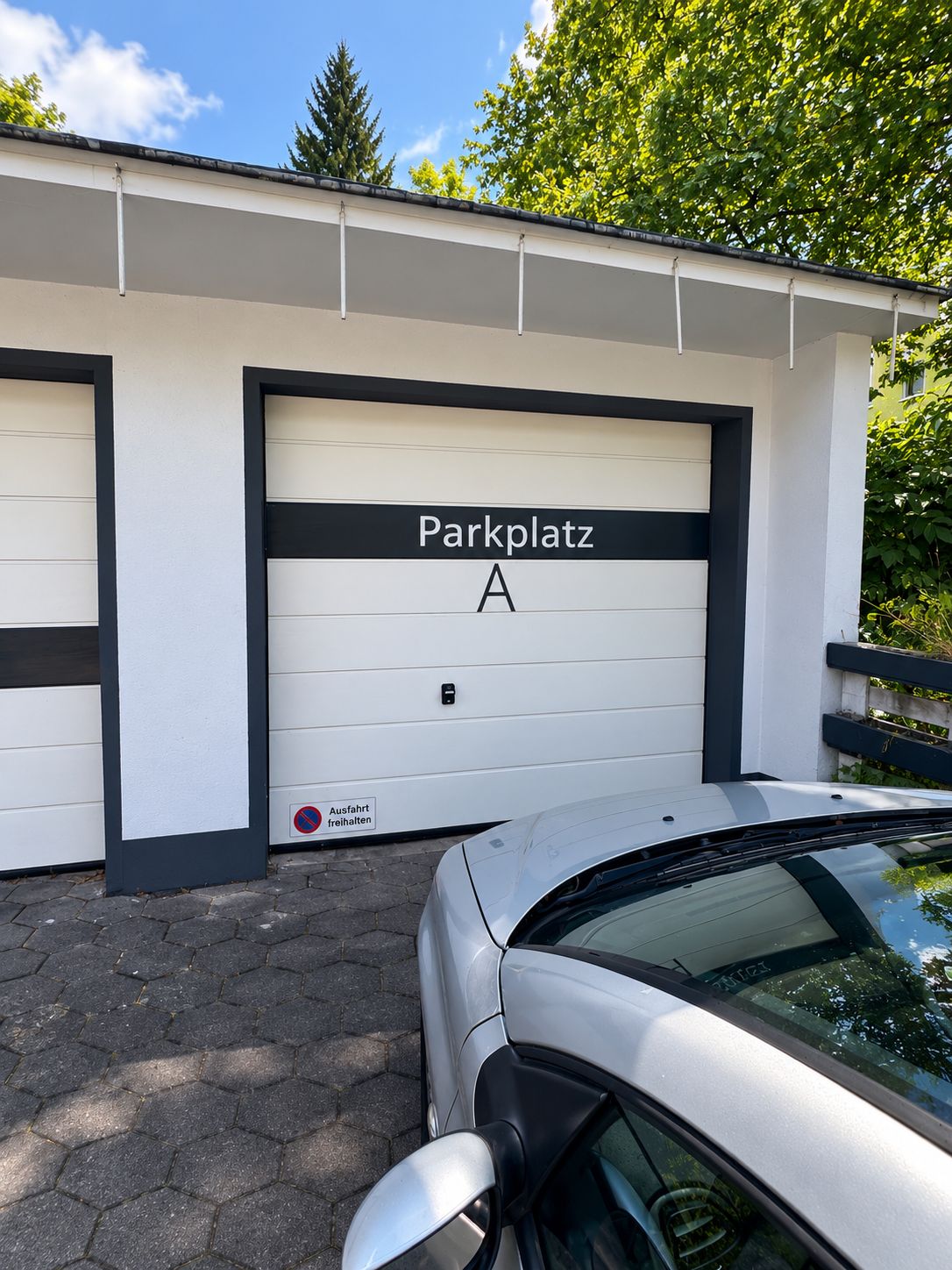 Een gebouw met een garage deur waarop 'Parkplatz A' staat, en een auto ervoor geparkeerd.