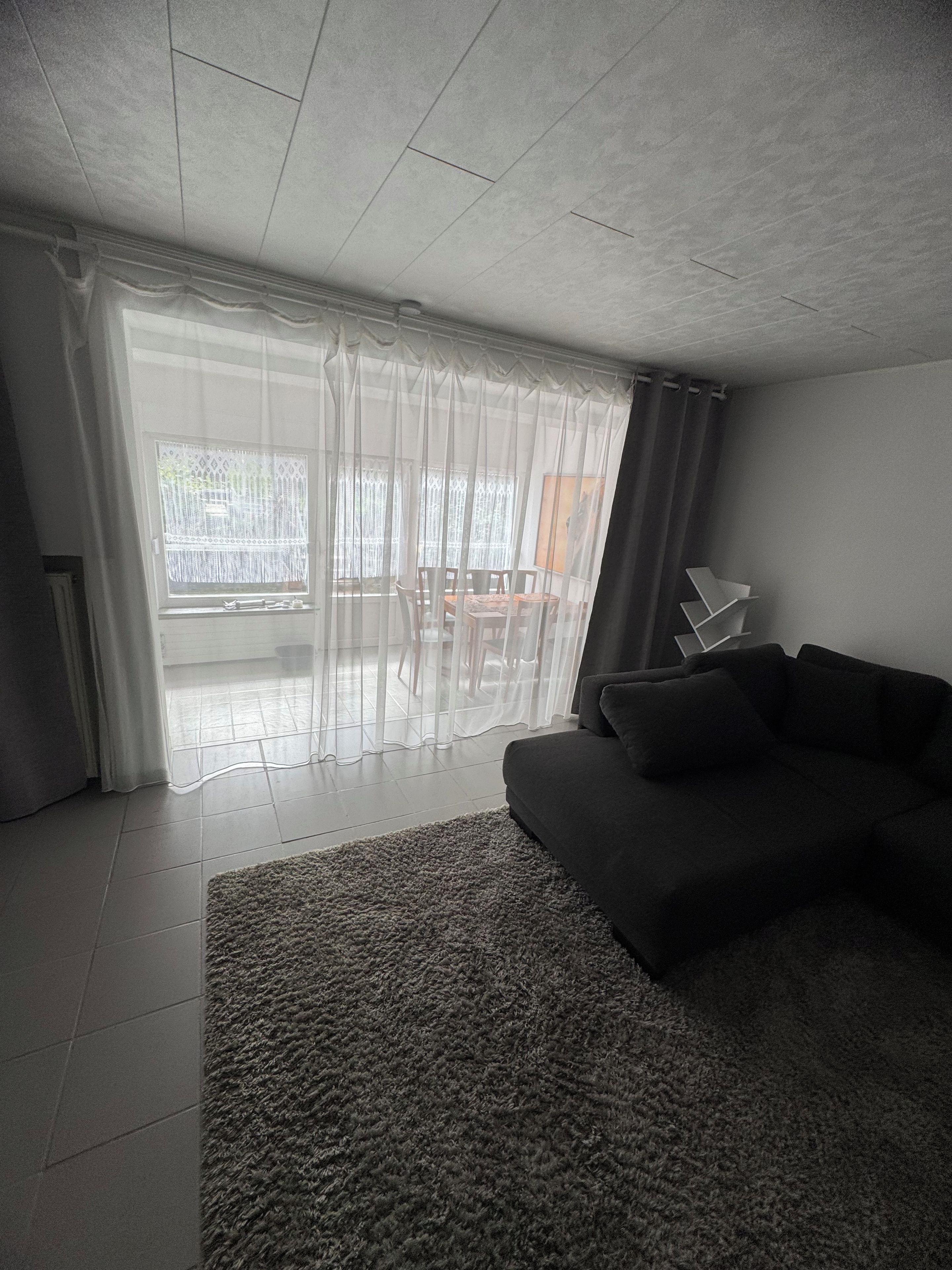 A modern living room with a dark sofa, a patterned rug, and sheer curtains.