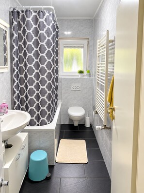 Et stilfuldt badeværelse med badekar, toilet, håndvask og et vindue.