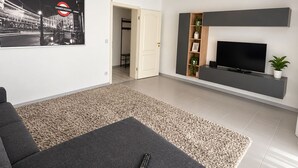 A modern living room with a grey sofa, a flat-screen TV, and a framed picture of a cityscape. - Spacious apartment with a parking space and a sunroom. (Iserlohn)