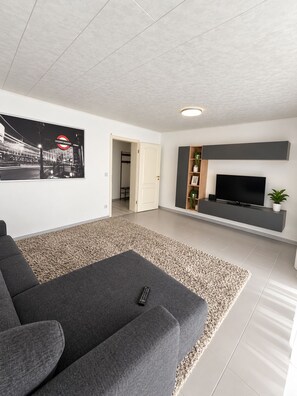 En moderne stue med en grå sofa, et fladskærms-tv og et indrammet billede af et bybillede.