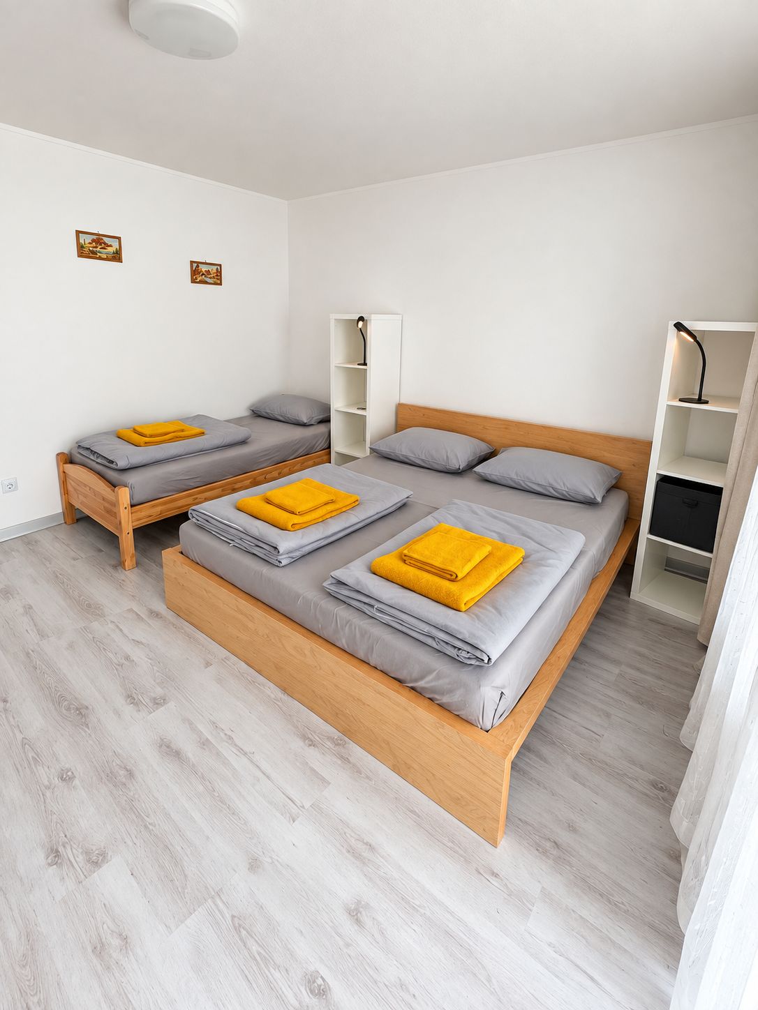 Ein Schlafzimmer mit zwei Betten, einem Holzkopfstück, einem weißen Wäscheschrank und einer kleinen Regaleinrichtung.