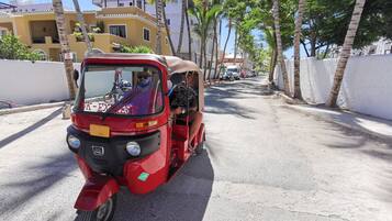 Un rickshaw rojo circulando por una calle con palmeras y edificios al fondo.