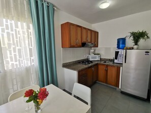 Une cuisine compacte avec des meubles de rangement en bois, une cuisinière à gaz, un four à micro-ondes et un réfrigérateur.