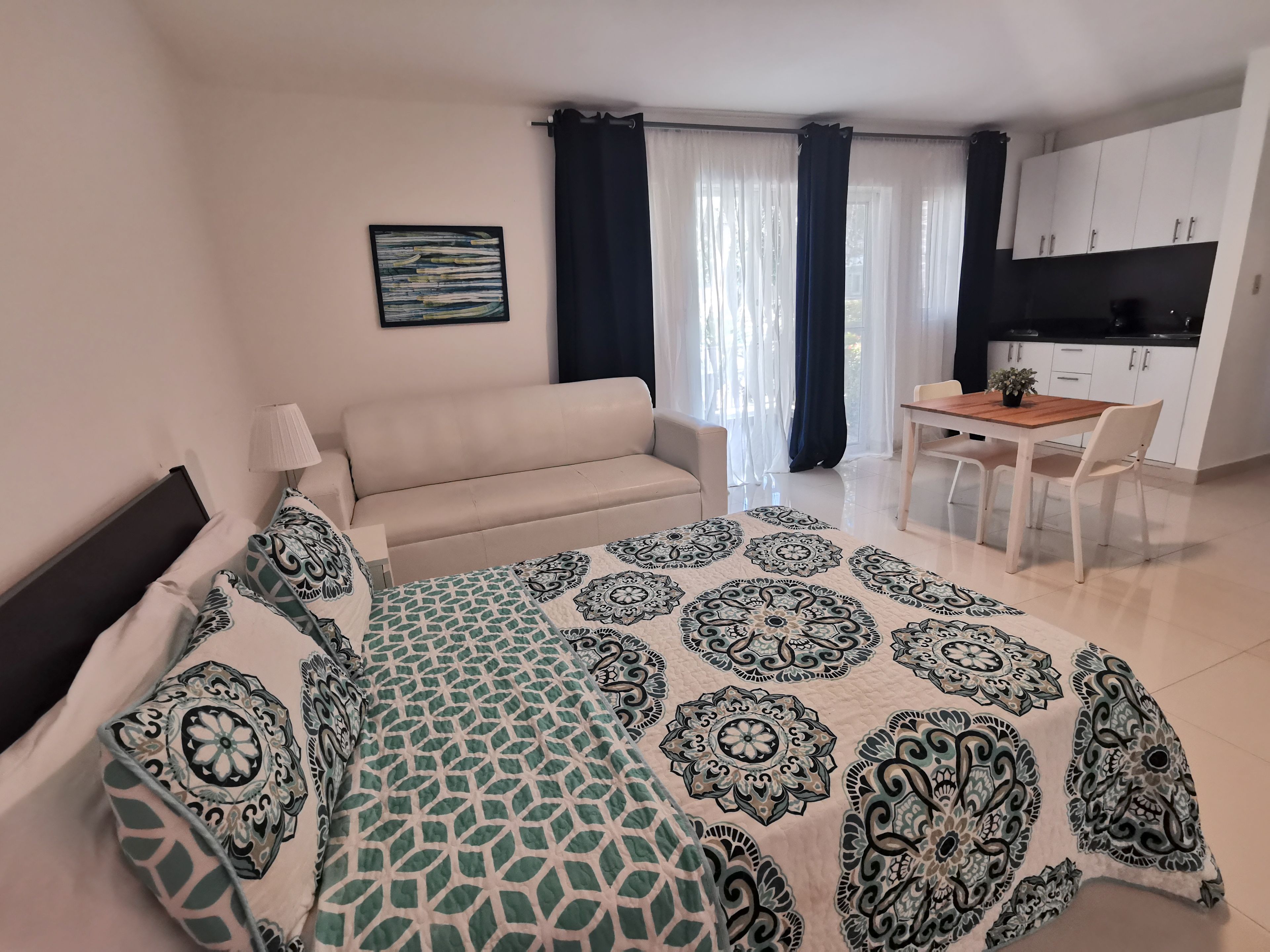 A modern bedroom with a bed, a sofa, a dining table with chairs, and a kitchenette.