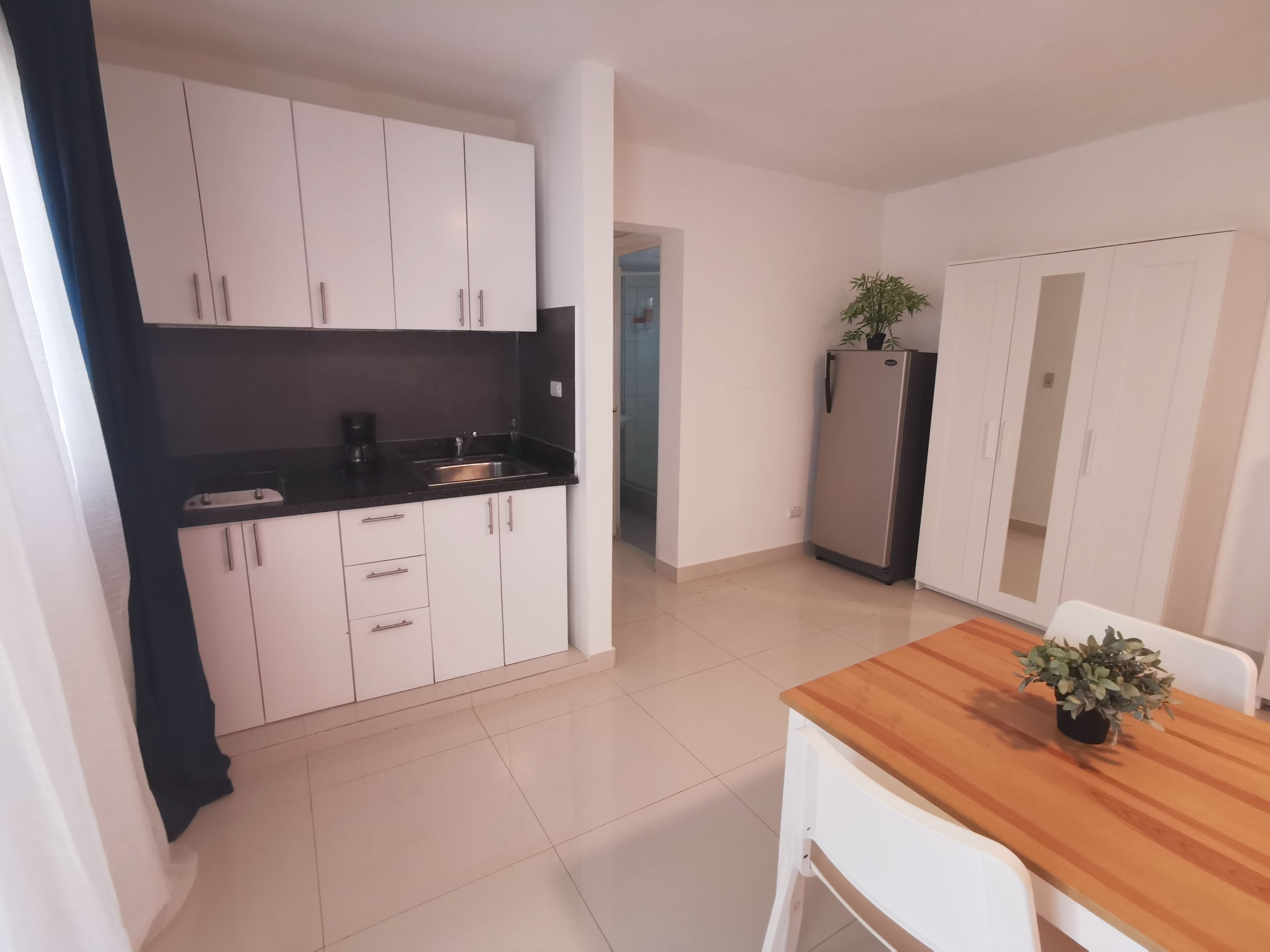 Cozinha compacta com armários brancos, bancada preta e geladeira de aço inoxidável.