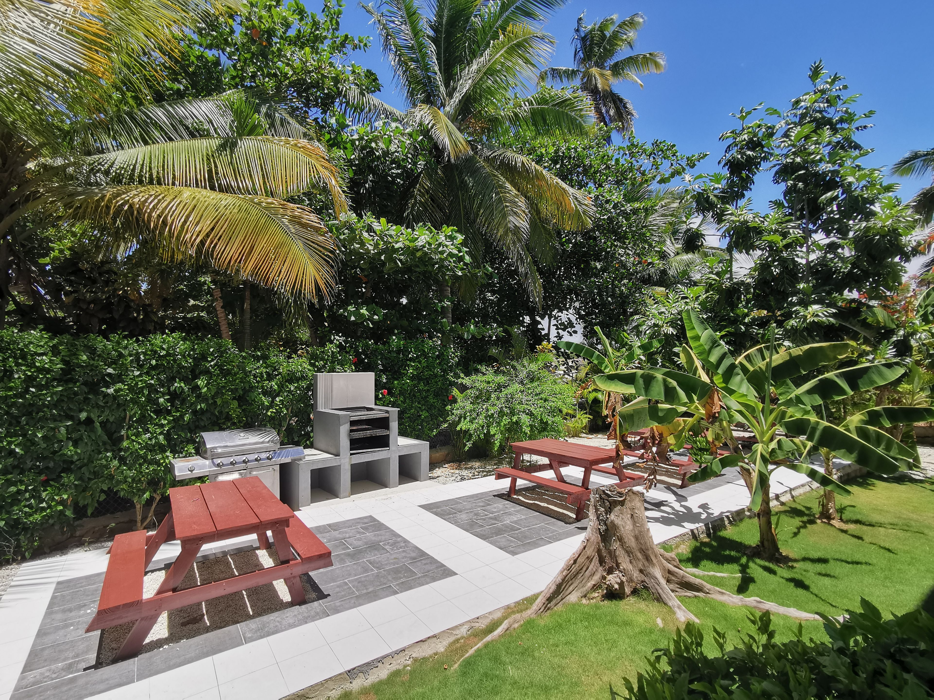 An outdoor patio area with a barbecue grill, seating, and a view of lush greenery.