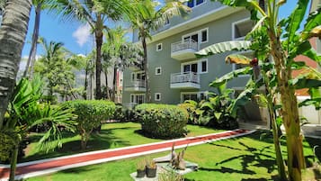 A residential building with a red pathway, lush greenery, and a clear blue sky.