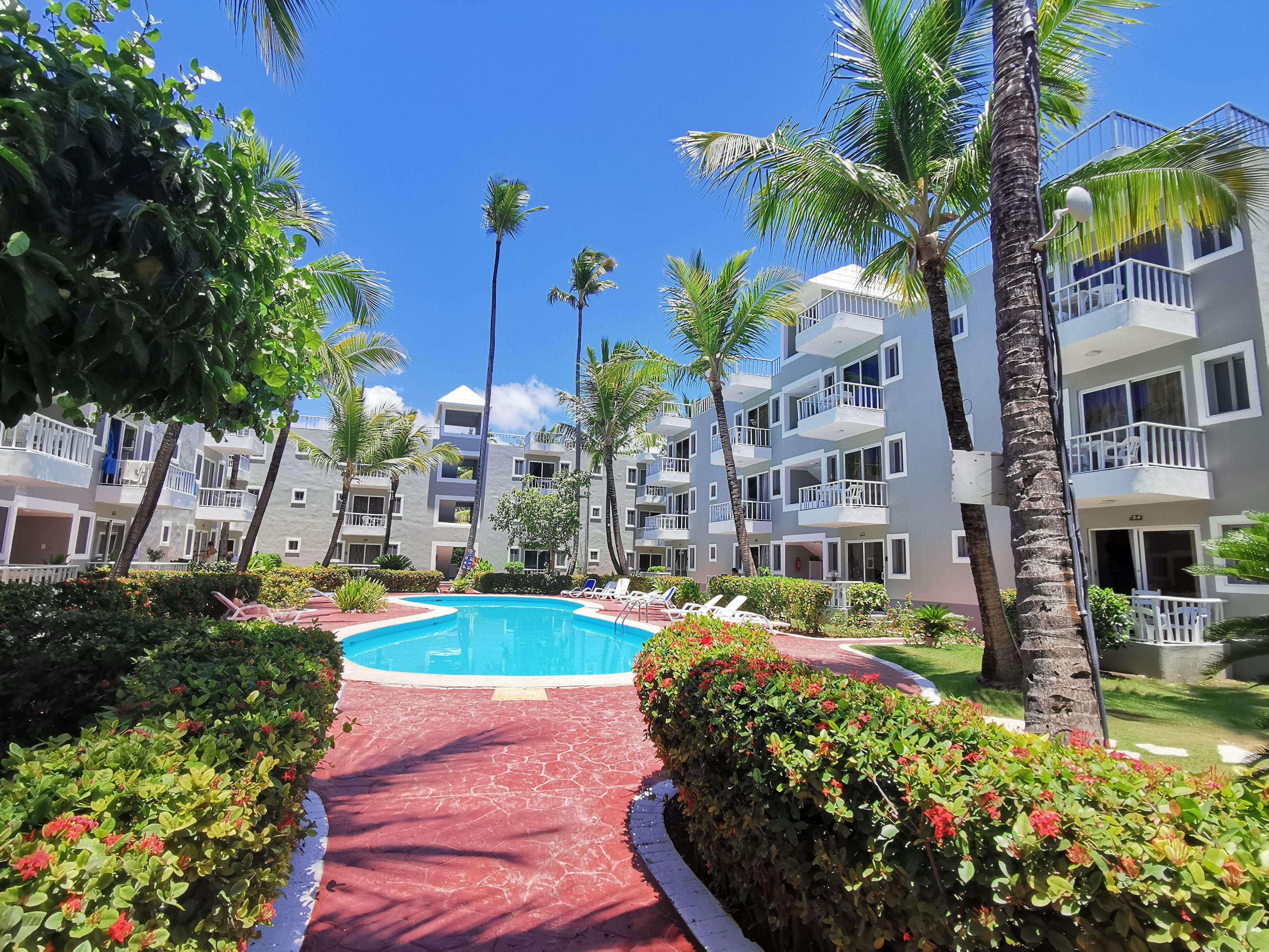 A resort with a swimming pool, palm trees, and a red pathway.