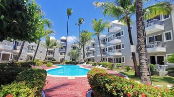 A resort with a swimming pool, palm trees, and a red pathway.