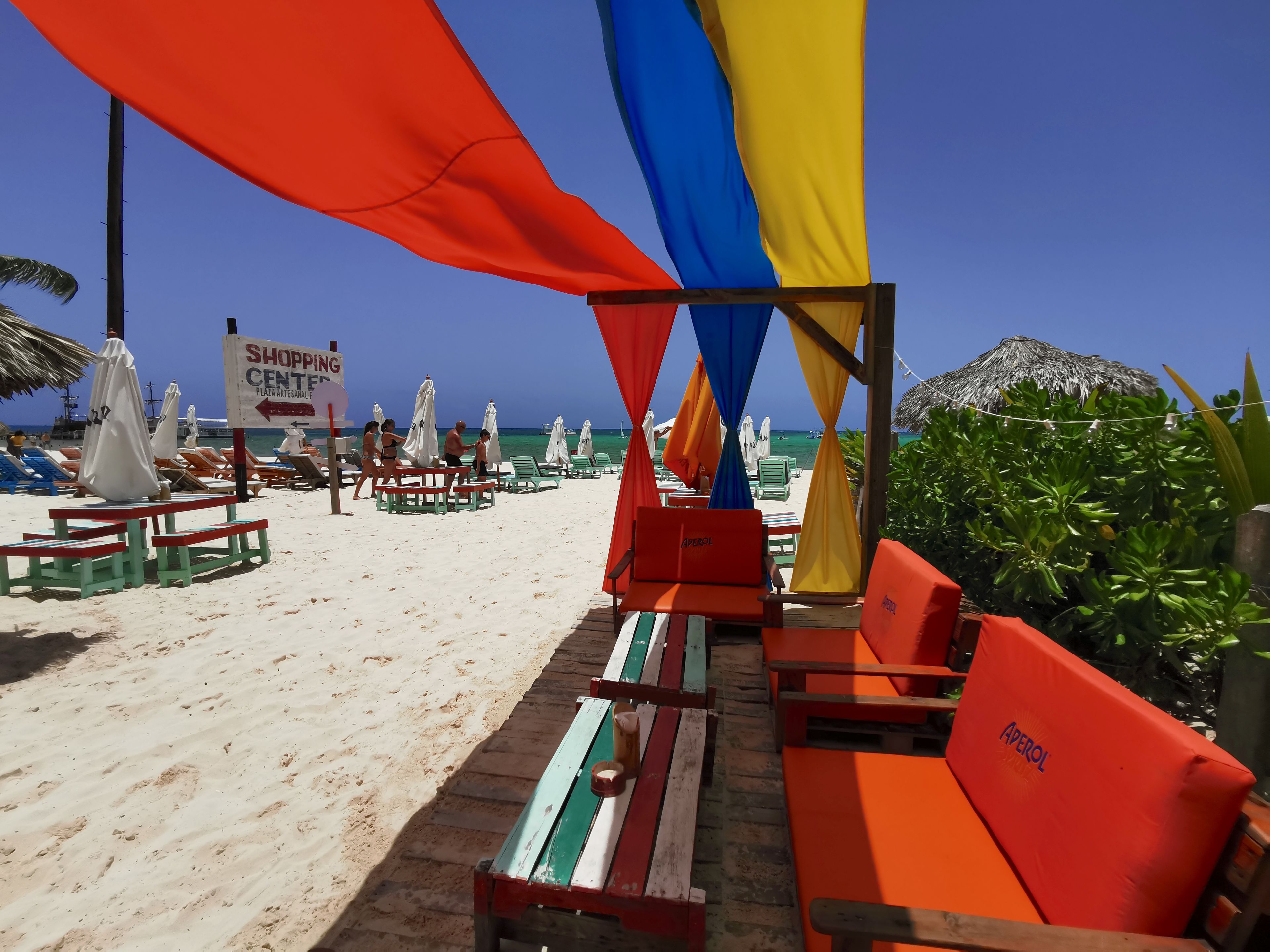 A beach with sun loungers, umbrellas, and a sign for a shopping center.