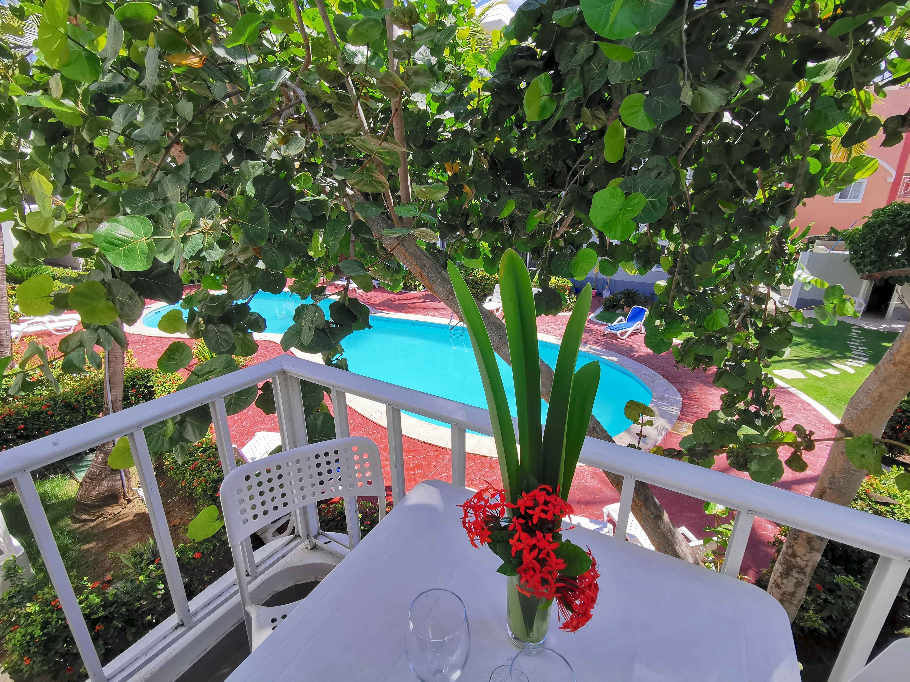 Ein Balkon mit Blick auf einen Swimmingpool, ein Tisch mit Blumenvase und ein Stuhl.