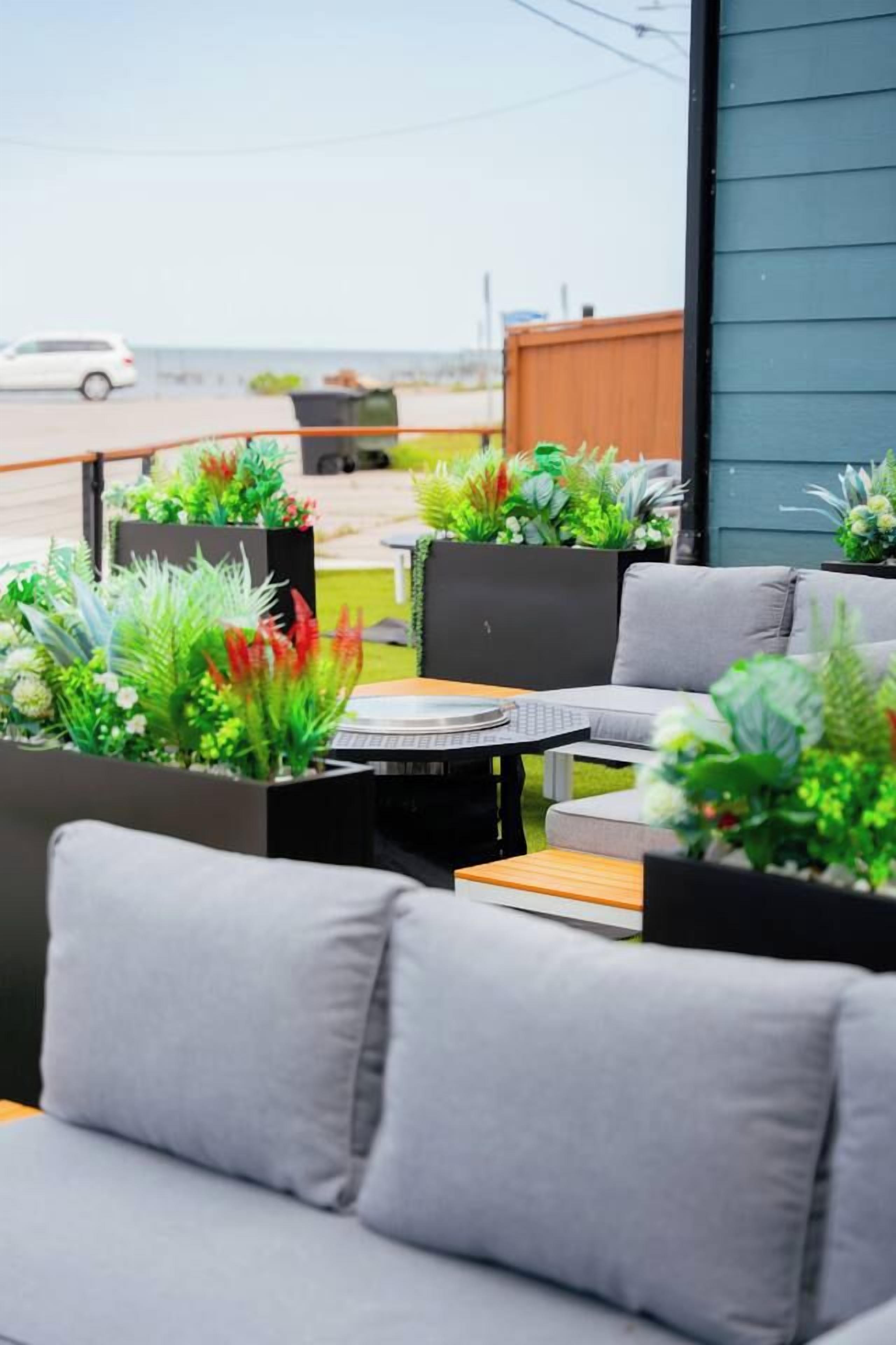 An outdoor seating area with grey sofas and a round table, surrounded by potted plants.