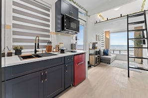 A modern kitchen with a built-in stove, a red refrigerator, and a view of the sea through large windows. - Galveston Bay Tiny Home | Loft & Shared Pool (Bacliff)