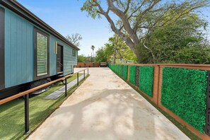 A pathway leading to a building with a blue exterior, surrounded by green artificial grass and a wooden fence.