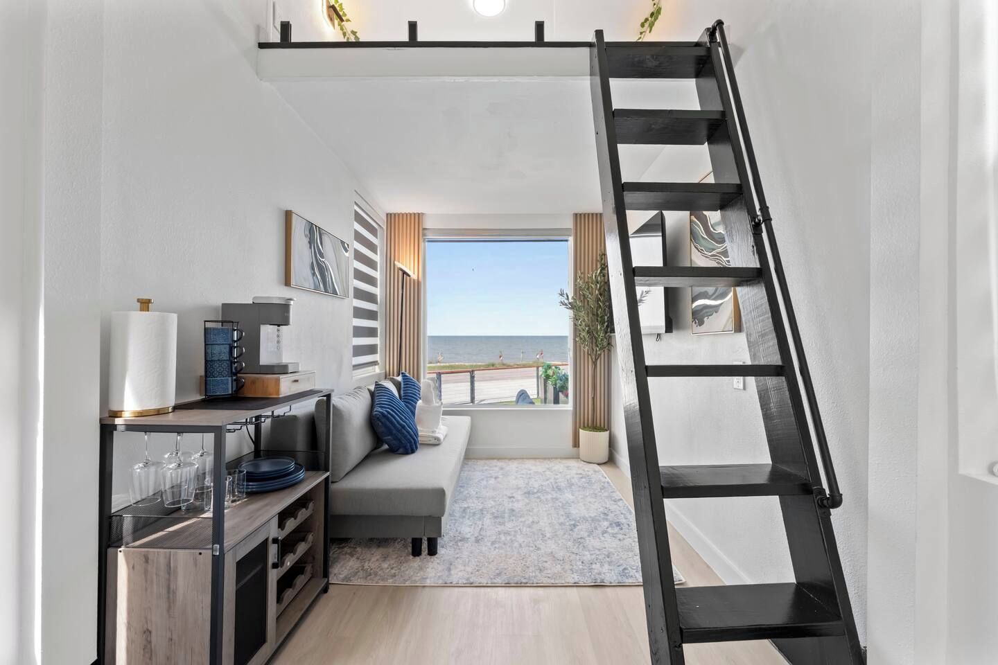 A compact living space with a loft area, a kitchenette, and a view of the sea.