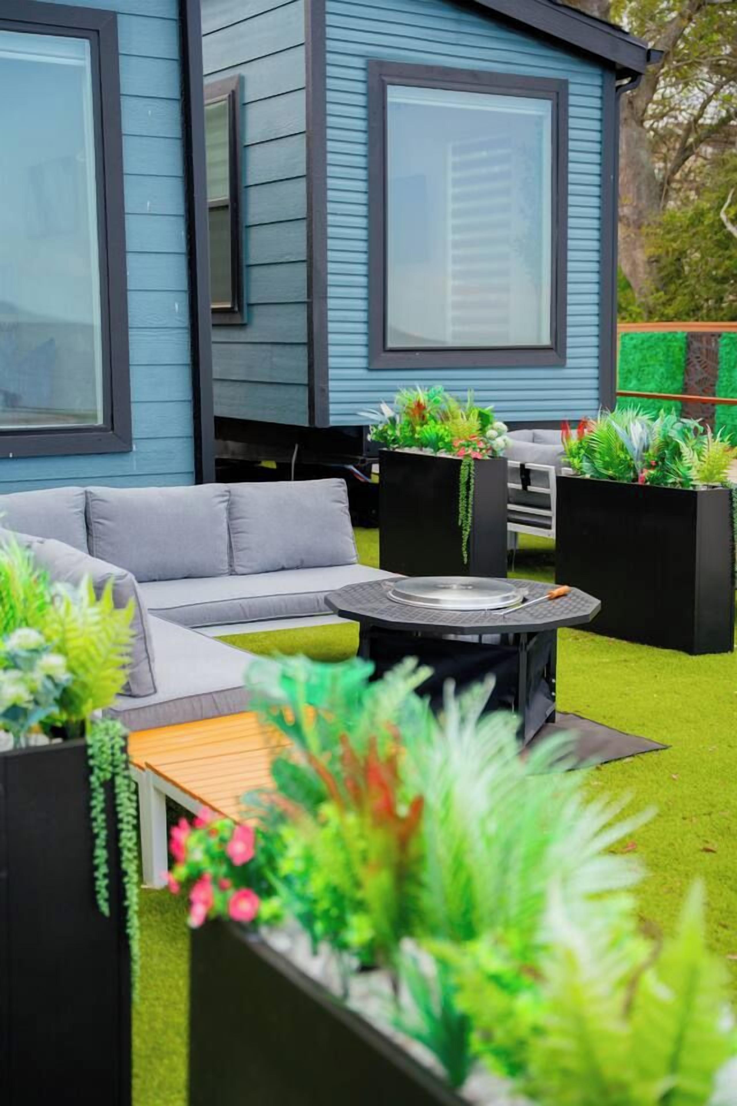 A modern outdoor seating area with a grey sofa, a round table, and black planters with greenery.