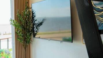 Une pièce dotée d’un grand téléviseur à écran plat fixé au mur, d’une plante en pot et d’une fenêtre avec des rideaux.