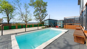 En swimmingpool med en træterrasse, en mindre bygning og havudsigt.
