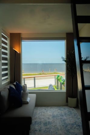 A room with a large window overlooking a beach and a road.