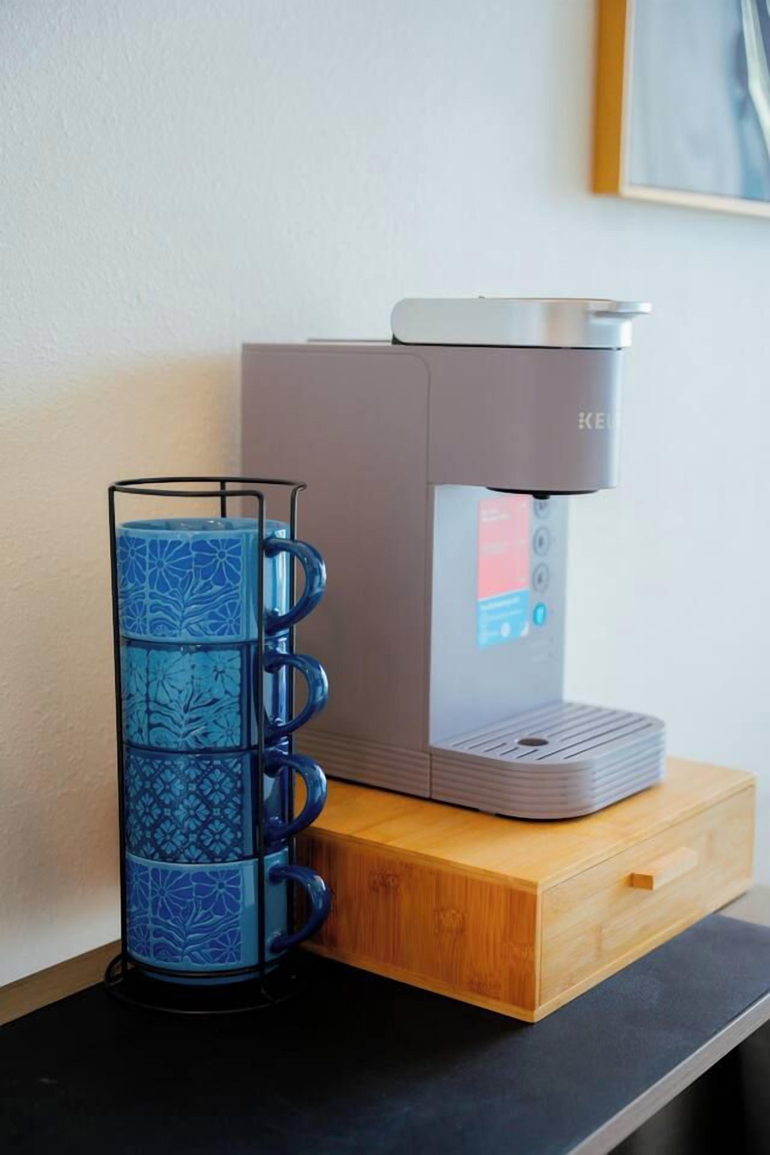 A coffee maker on a wooden counter with a blue mug holder beside it.