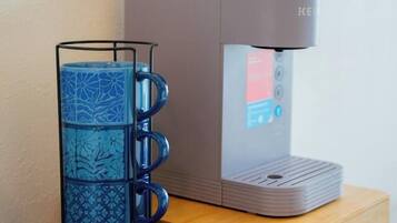 A coffee maker on a wooden counter with a blue mug holder beside it.