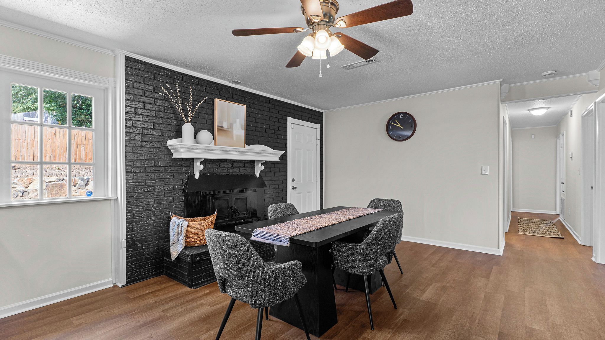 A dining area with a black table, four chairs, a ceiling fan, and a fireplace.