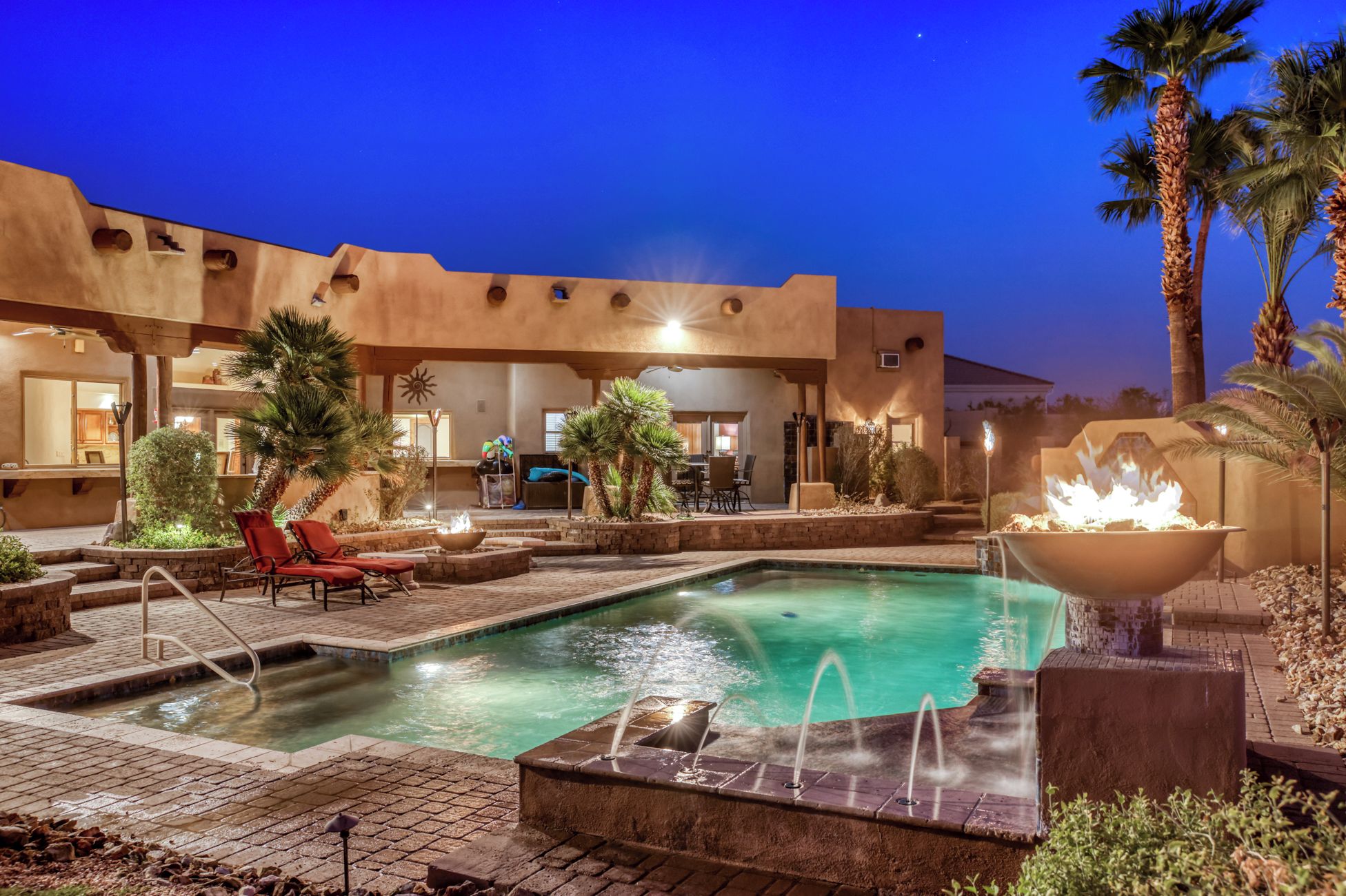 A pool area with a fire feature, lounge chairs, and palm trees.