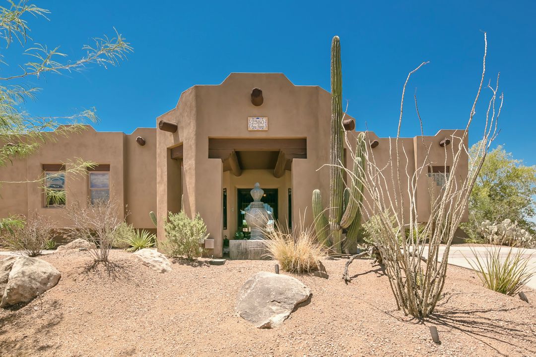 Un edificio de techo plano, entrada central y jardín árido con cactus y rocas.