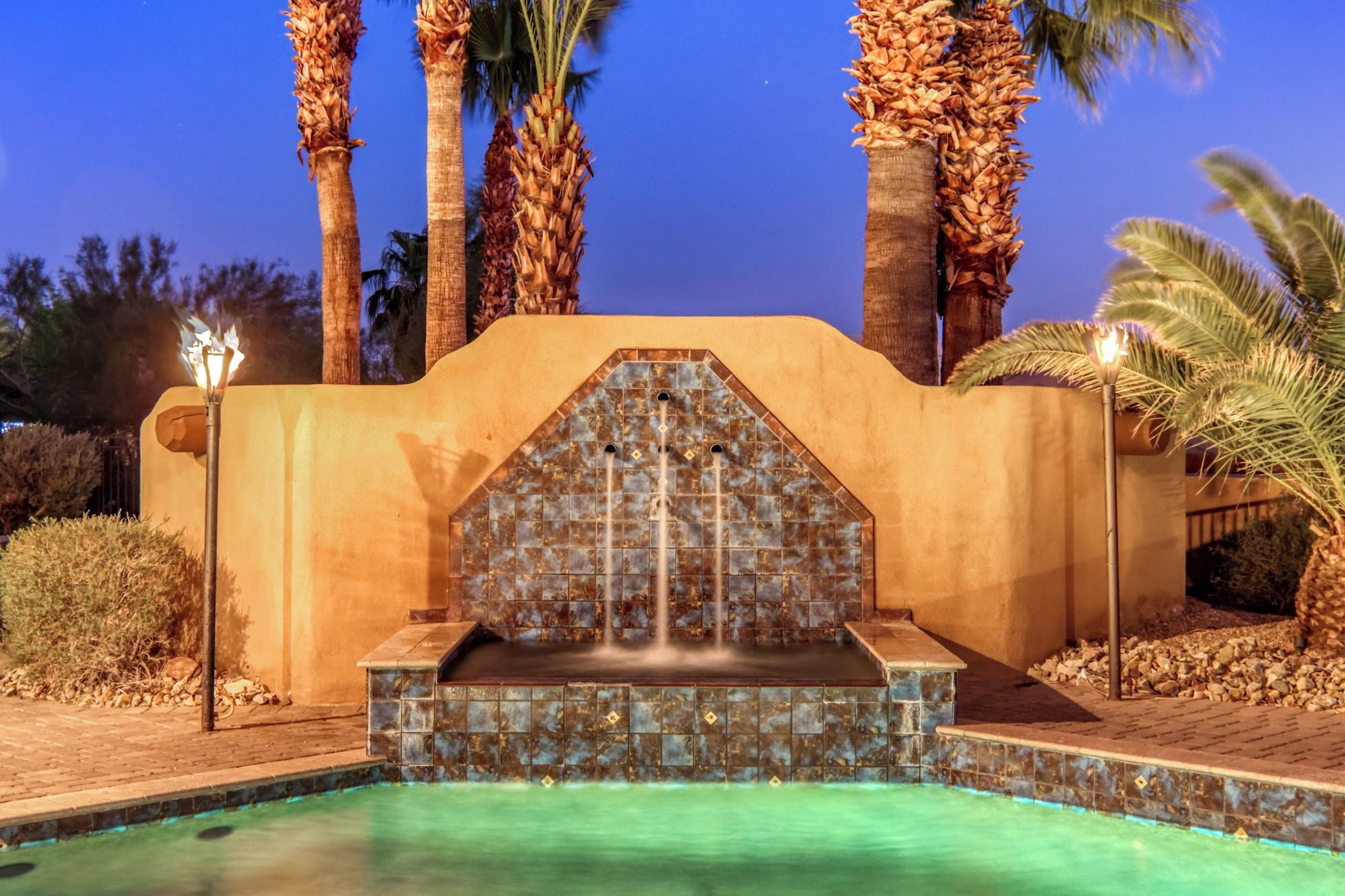 A pool area with a tiled waterfall feature, surrounded by palm trees and a night sky.