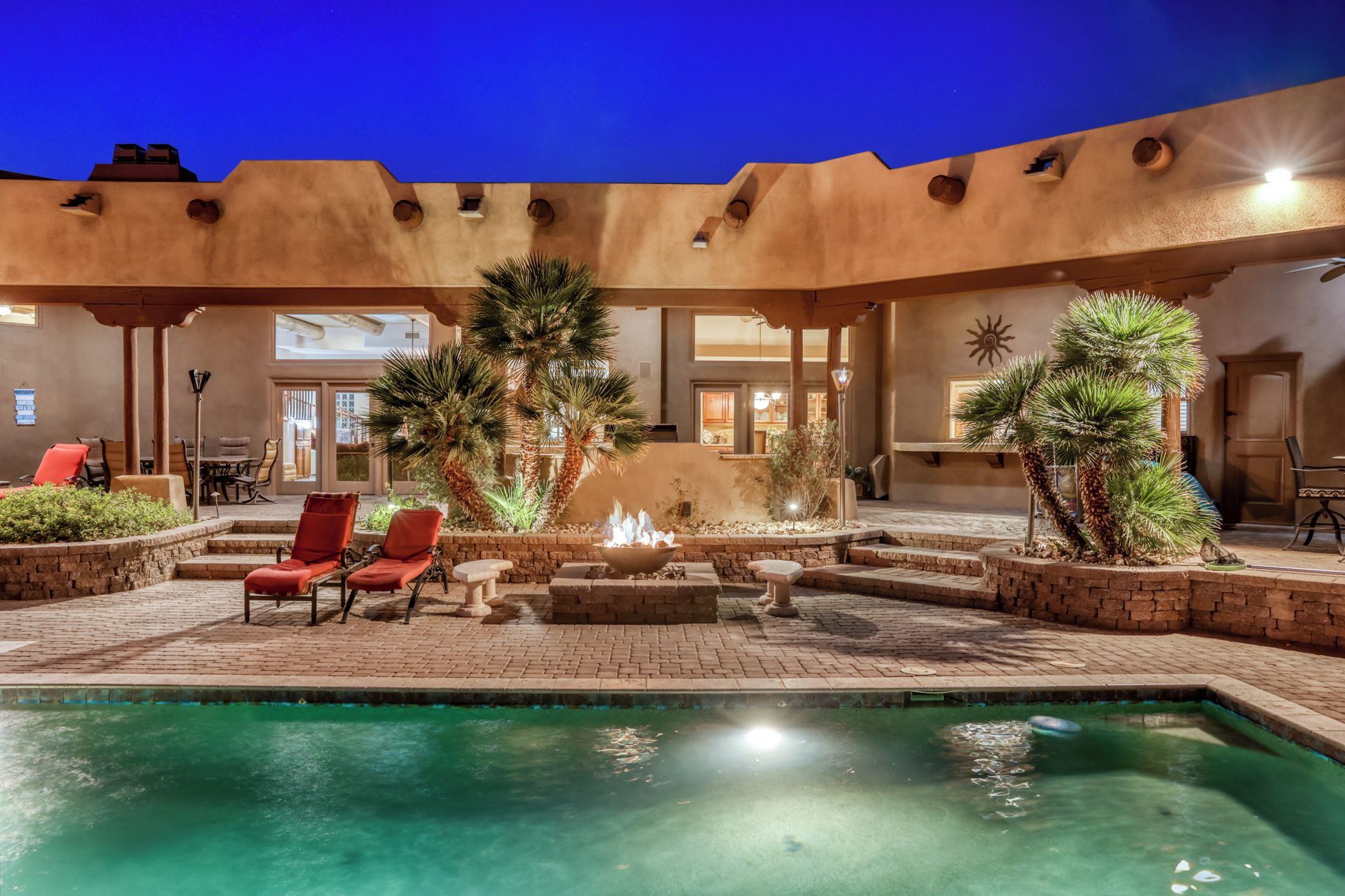 A pool area with red chairs, a fire feature, and palm trees.