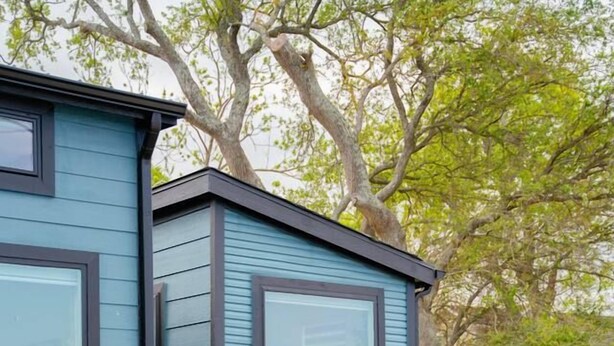 A modern outdoor seating area with a blue building, green plants, and a wooden table. - Waterfront Tiny Suite | Cal King + Bay Views|Kemah (Bacliff)