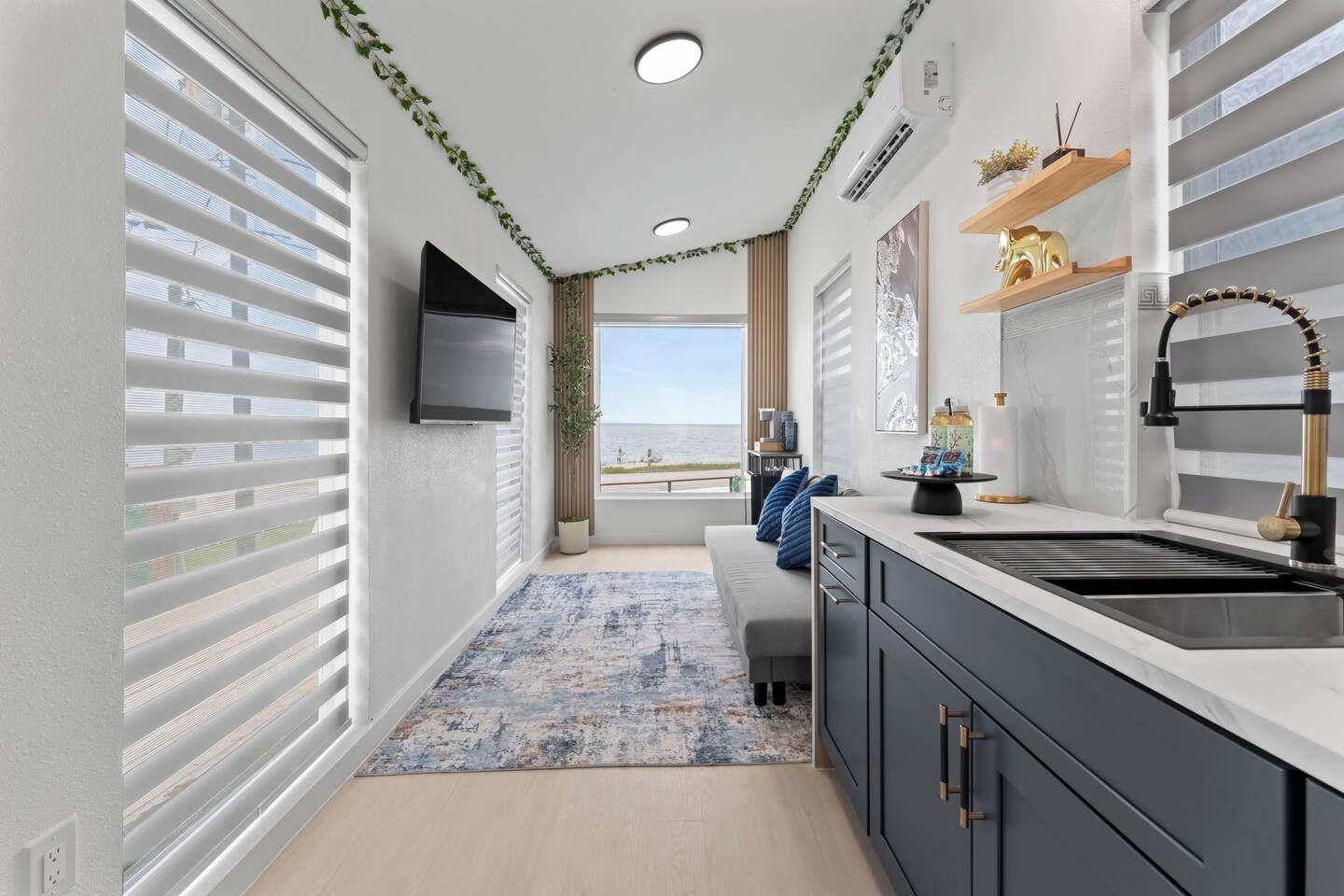 A modern kitchen with a built-in sink, a flat-screen TV, and a view of the sea.