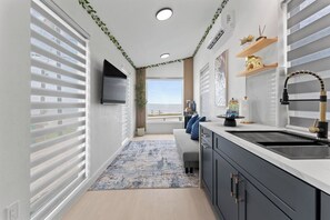 A modern kitchen with a built-in sink, a flat-screen TV, and a view of the sea.