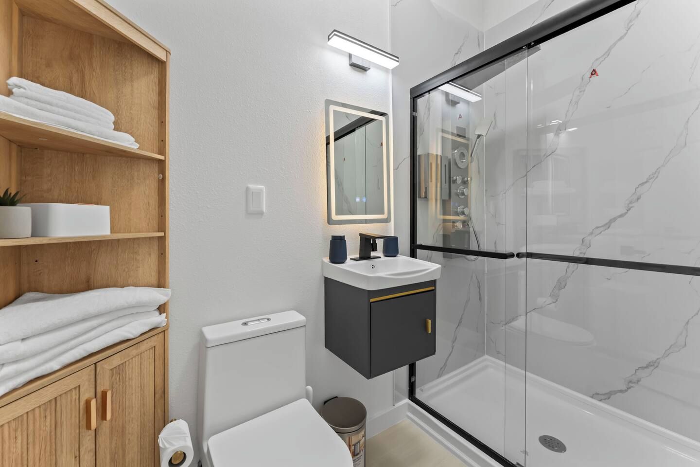 Ein modernes Badezimmer mit Duschkabine aus Glas, einem Holzausziehtisch und einer weißen Toilette.