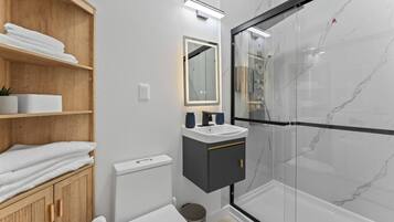 Ein modernes Badezimmer mit Duschkabine aus Glas, einem Holzausziehtisch und einer weißen Toilette.