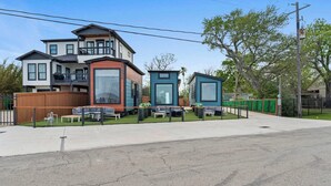 A residential area with a two-story house and two single-story structures, a paved driveway, and outdoor seating. - Waterfront Tiny Suite | Cal King + Bay Views|Kemah (Bacliff)