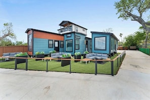 Una casa moderna con techo plano, balcón y patio trasero cercado con mobiliario exterior.