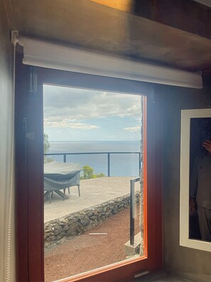 A room with a view of a body of water, a covered outdoor table, and a stone wall. - Mint and Honey - Azorean architecture with modern elegance and a 180° ocean view (Lajes do Pico)
