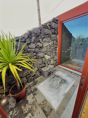 A stone wall, a potted plant, a glass door, and a tiled floor. - Mint and Honey - Azorean architecture with modern elegance and a 180° ocean view (Lajes do Pico)