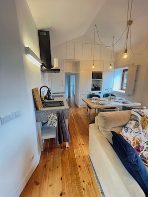 A modern kitchen with white cabinetry, a built-in oven, and a dining area with a table set for four. - Mint and Honey - Azorean architecture with modern elegance and a 180° ocean view (Lajes do Pico)
