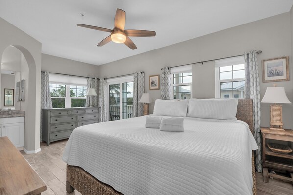 A bedroom with a large bed, a ceiling fan, and a view of the outdoors through the windows. - Turtle Tales on Anna Maria I Pool & Hot Tub I Bermuda Bay Club (Bradenton Beach)