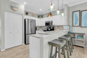 A modern kitchen with white cabinetry, stainless steel appliances, and a central island with bar stools. - Turtle Tales on Anna Maria I Pool & Hot Tub I Bermuda Bay Club (Bradenton Beach)