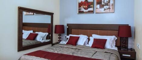 A hotel room with a large bed, two bedside tables, a mirror, and two wall-mounted artworks.