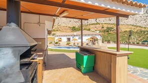 Ein Grillplatz im Freien mit einem Grill, einer grünen Mülltonne und einem Pool im Hintergrund.